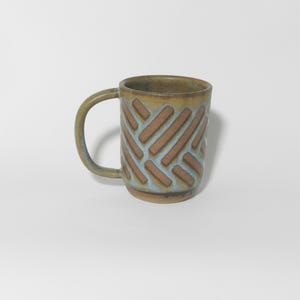 May include: A ceramic mug with a unique design. The mug features a brown and blue geometric pattern on a light brown background. It has a curved handle and is suitable for hot or cold beverages.
