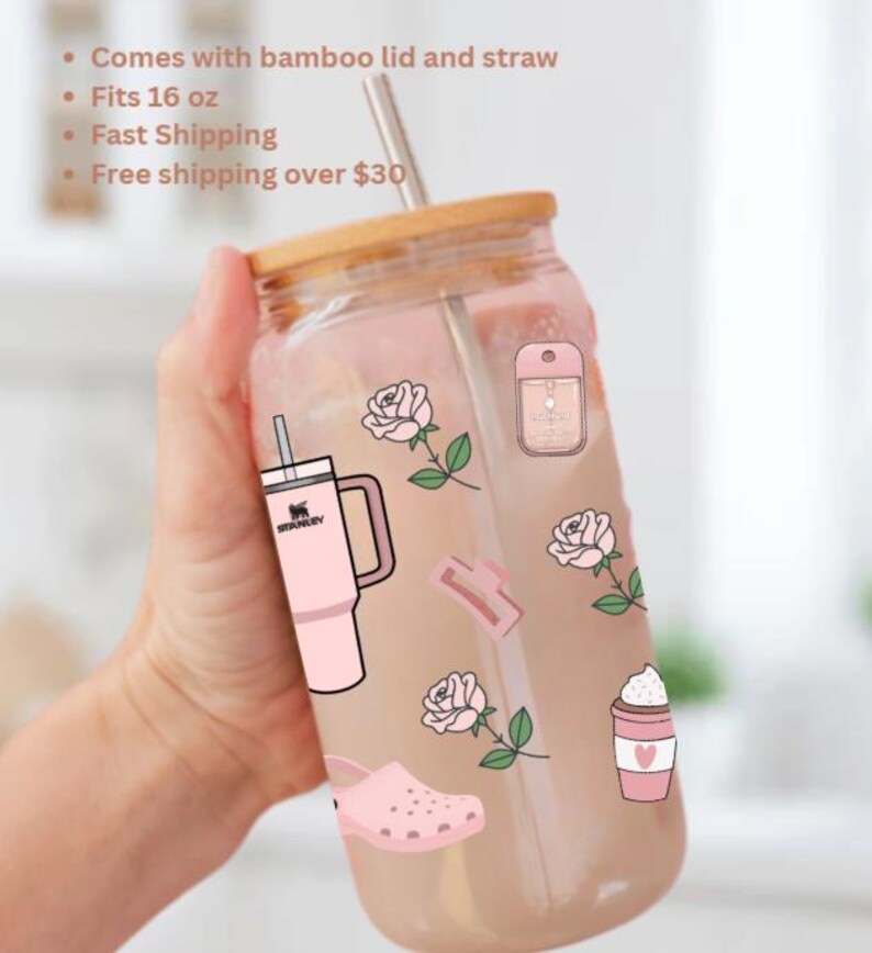 May include: A clear glass tumbler with a bamboo lid and straw, decorated with pink stickers of roses, a Stanley tumbler, a coffee cup, and other pink accessories. The tumbler fits 473 ml.