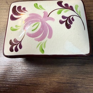Könnte beinhalten: Rechteckige Keramikschale mit floralem Design. Die Schale hat einen weißen Hintergrund mit Craquelé-Effekt und ist mit einer großen rosa Blume, grünen Blättern und dunkelvioletten Akzenten verziert. Die Ränder sind dunkelviolett.
