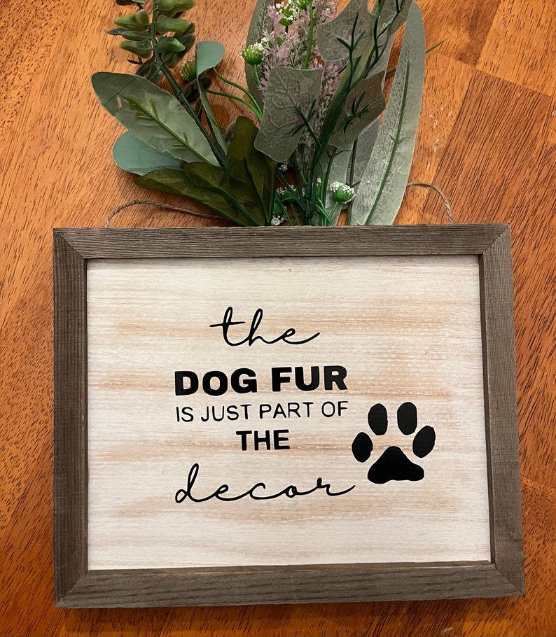 May include: A rustic wooden sign with a white background and black text that reads "the dog fur is just part of the decor" with a black paw print to the right of the text.