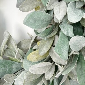 May include: A close-up of a wreath made of faux lambs ear leaves. The leaves are a light green color and have a fuzzy texture.