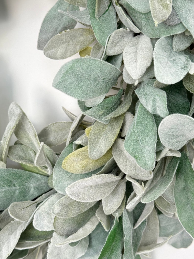 May include: A close-up of a wreath made of faux lambs ear leaves. The leaves are a light green color and have a fuzzy texture.