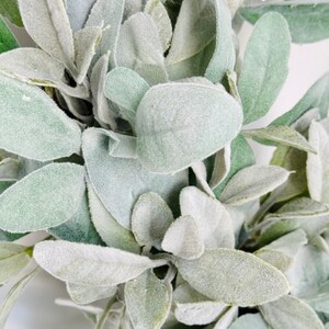 May include: Close-up of a wreath made of faux lambs ear leaves. The leaves are a light green color and have a fuzzy texture.