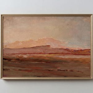 May include: An oil painting of a landscape with a gold frame. The artwork depicts a muted color palette of browns, reds, and beige, suggesting a sunset or sunrise over a mountainous terrain. The brushstrokes are visible, adding texture.