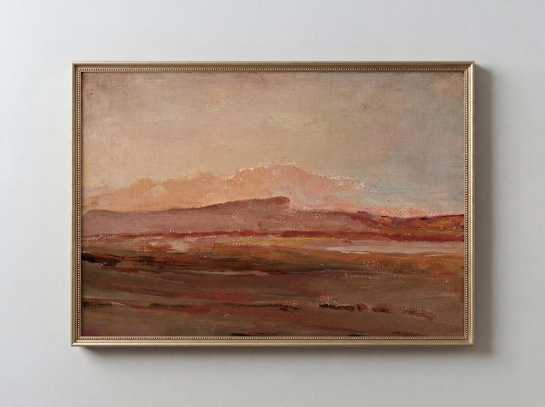 May include: An oil painting of a landscape with a gold frame. The artwork depicts a muted color palette of browns, reds, and beige, suggesting a sunset or sunrise over a mountainous terrain. The brushstrokes are visible, adding texture.