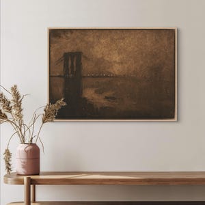 May include: A sepia-toned print of the Brooklyn Bridge at night, with the bridge's silhouette outlined against a dark sky. The water below the bridge is dark, and there are lights visible on the bridge and in the distance.