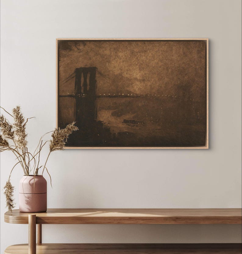May include: A sepia-toned print of the Brooklyn Bridge at night, with the bridge's silhouette outlined against a dark sky. The water below the bridge is dark, and there are lights visible on the bridge and in the distance.