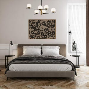 May include: A gray upholstered bed with white bedding and a black throw blanket. Two black table lamps with white shades are on either side of the bed. A black and white abstract painting hangs above the headboard. A modern chandelier with five white globe lights hangs from the ceiling.