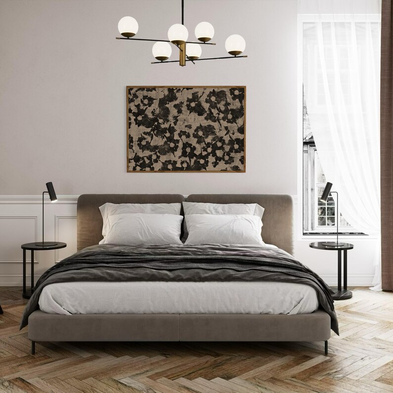 May include: A gray upholstered bed with white bedding and a black throw blanket. Two black table lamps with white shades are on either side of the bed. A black and white abstract painting hangs above the headboard. A modern chandelier with five white globe lights hangs from the ceiling.