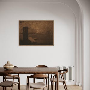 May include: A framed sepia-toned print of a bridge over a body of water. The print is hanging on a white wall above a wooden dining table with chairs.
