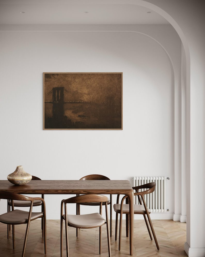 May include: A framed sepia-toned print of a bridge over a body of water. The print is hanging on a white wall above a wooden dining table with chairs.