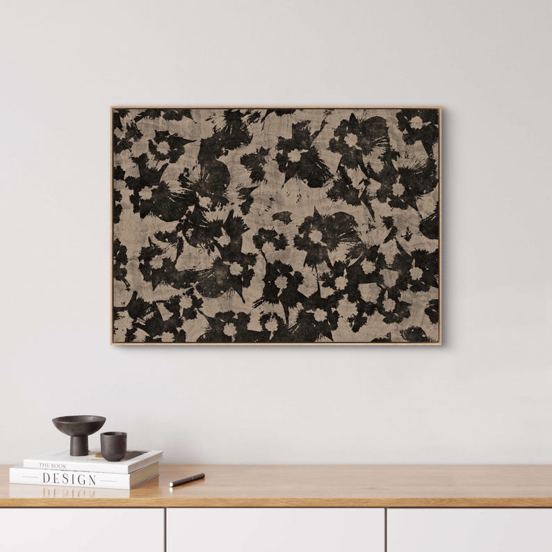 May include: Abstract art print with a black and white floral pattern on a beige background. The print is framed in a light wood frame.