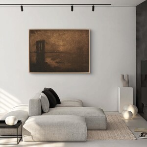 May include: A framed sepia-toned painting of a bridge over water. The bridge is silhouetted against a hazy sky. The painting is hanging on a white wall in a modern living room.