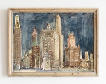 May include: Watercolor painting of a cityscape featuring tall buildings in shades of brown, beige, and gold, set against a dark blue sky. The artwork is framed in a light brown wooden frame.