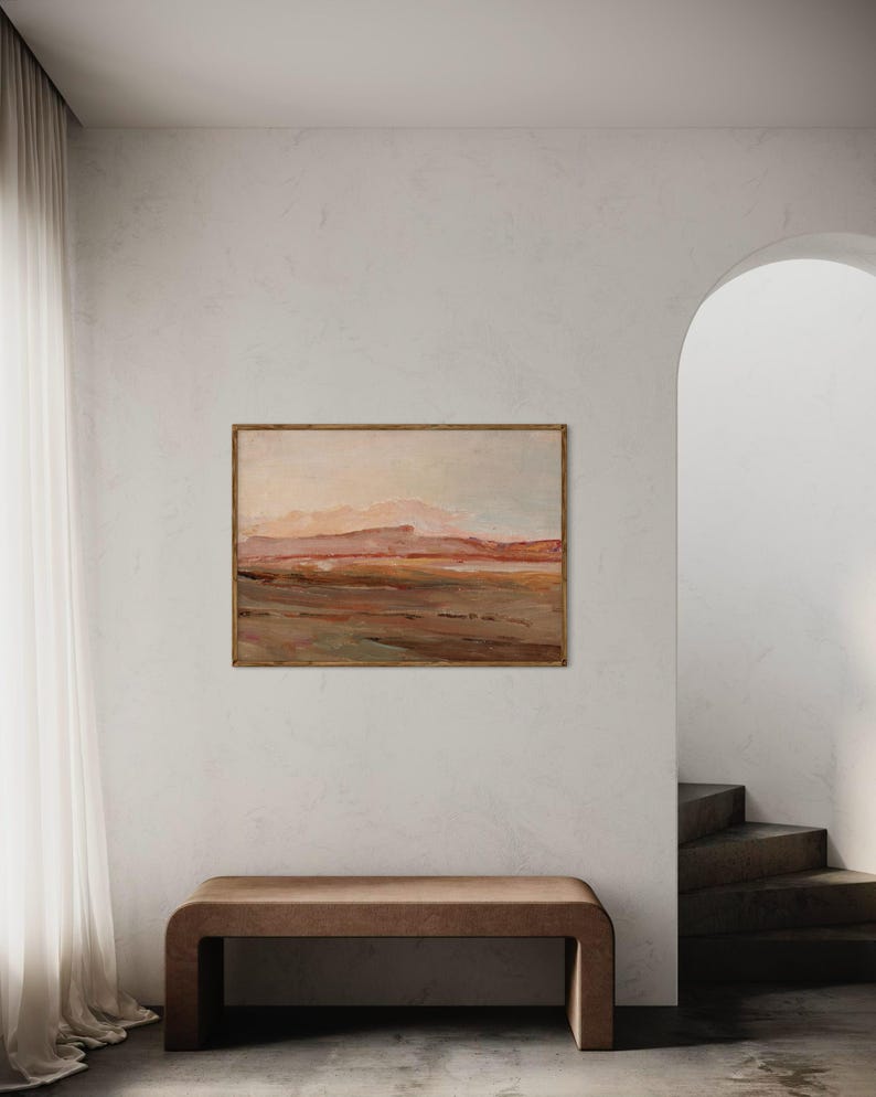 May include: An abstract landscape painting in a wooden frame hangs above a brown bench. The artwork features warm tones of brown, orange, and pink, depicting a mountainous terrain. The room has a neutral color palette with a white wall and a sheer curtain.