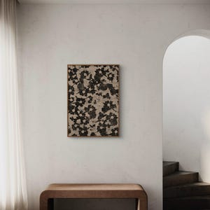 May include: A brown wooden bench with a beige floral print framed artwork hanging on the wall behind it. The artwork is in a light wood frame. The wall is a light beige color. The bench is in a room with a white ceiling and a white floor.