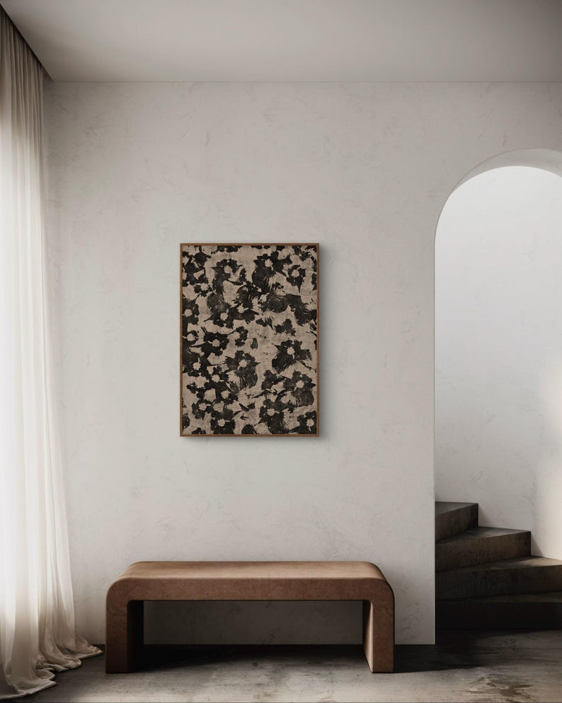 May include: A brown wooden bench with a beige floral print framed artwork hanging on the wall behind it. The artwork is in a light wood frame. The wall is a light beige color. The bench is in a room with a white ceiling and a white floor.