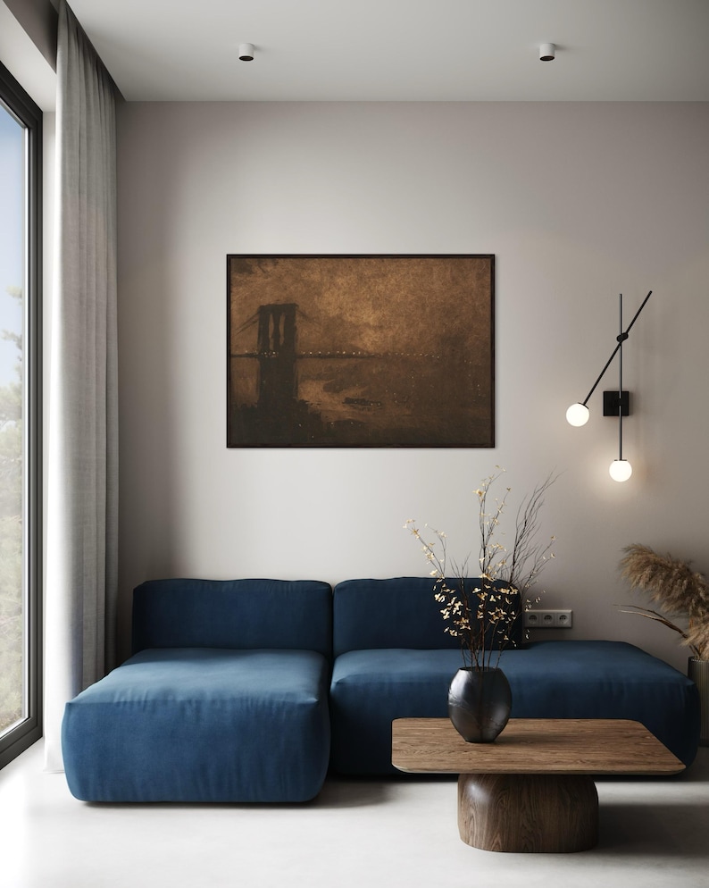 May include: A blue sectional sofa with a wooden coffee table in front of it. A vase with dried flowers sits on the table. A framed print of a bridge over water hangs on the wall behind the sofa.