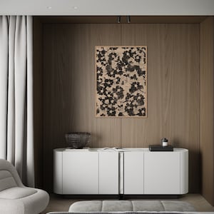 May include: A white cabinet with three doors and a black metal divider. The cabinet is sitting on a wooden floor in front of a wall with a black and white floral print framed artwork. A black wire basket and a black tray with a bottle are on top of the cabinet.