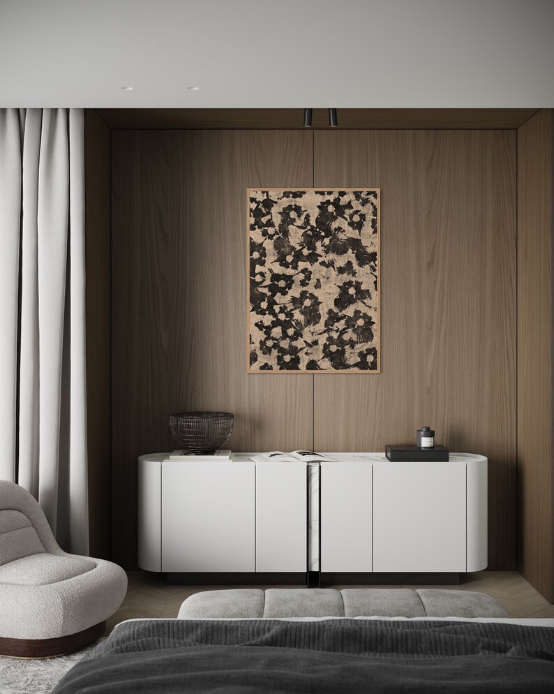 May include: A white cabinet with three doors and a black metal divider. The cabinet is sitting on a wooden floor in front of a wall with a black and white floral print framed artwork. A black wire basket and a black tray with a bottle are on top of the cabinet.