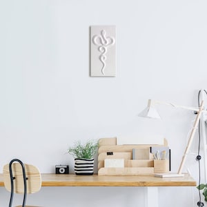 Op de afbeelding: Witte keramische wandkunst met een reli&euml;f van een slang. De slang staat verticaal met zijn kop bovenaan en zijn staart onderaan. De slang is opgerold in een spiraalvorm.