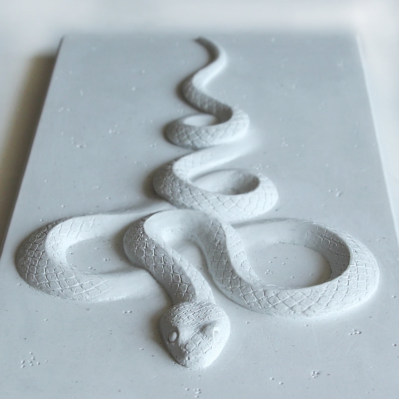 Op de afbeelding: Een wit, getextureerd, slangensculptuur in een opgerolde positie. De slang is gemaakt van een materiaal dat lijkt op beton of gips.