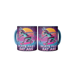 May include: Two blue mugs with a retro 80s design. Each mug features a pink donkey skateboarding with a sunset and palm trees in the background. The text "Skate Fast, Eat Ass" is printed on the mugs.