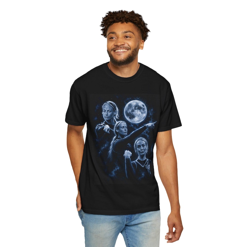 May include: A black short-sleeved t-shirt featuring a blue-toned graphic print of three figures in various poses against a dark, starry background with a large, glowing full moon. The figures are rendered in a monochromatic blue artistic style.