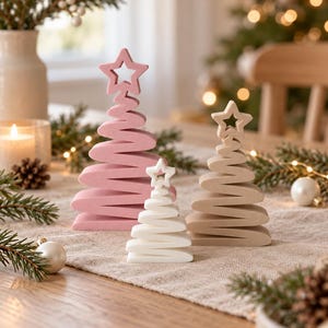 May include: Three decorative Christmas tree ornaments in varying sizes and colors. The largest is pink, the medium is beige, and the smallest is white. Each tree features a spiral, ribbon-like design topped with a cutout star shape.