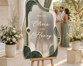 Può includere: Un cartello nuziale ad arco con un pannello centrale smerigliato che riporta il testo FOREVER Olivia AND Henry 10.02.2026. La cornice ha una finitura dorata con accenti in marmo verde scuro e dettagli a coste, su un cavalletto in legno.