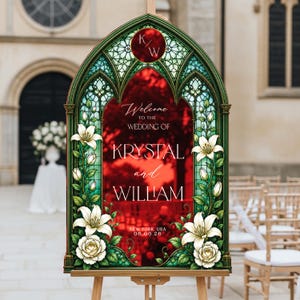 K&ouml;nnte beinhalten: Ein bogenf&ouml;rmiges Hochzeits-Willkommensschild mit einem Buntglasrahmen in Gr&uuml;nt&ouml;nen, verziert mit Illustrationen wei&szlig;er Lilien und Rosen. In der Mitte steht der Text: Welcome to the wedding of Krystal and William, New York, USA, 06.06.26, sowie ein K/W-Monogramm.