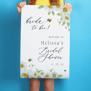 May include: A white bridal shower sign with the text "Bride to bee!" and "Melissa's Bridal Shower" in elegant script. The sign is decorated with watercolor daisies and bees. The date 11.25.25 is also included.