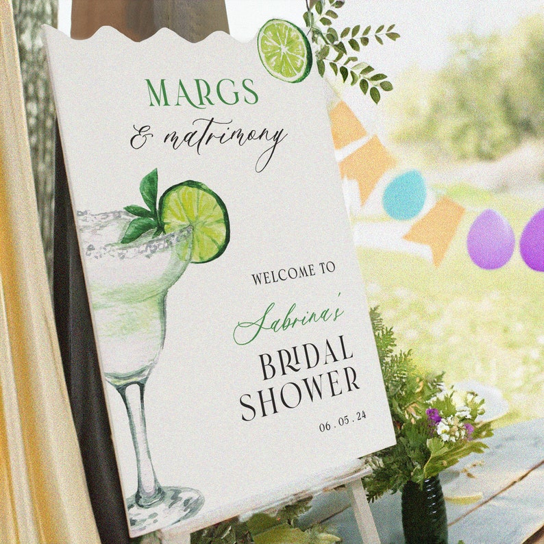 May include: A white sign with green text and a watercolor illustration of a margarita glass with a lime wedge. The text reads "Margs & Matrimony" and "Welcome to Sabrina's Bridal Shower 06.03.24".