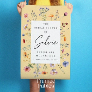 May include: A rectangular poster with a light yellow background featuring a white central panel. The text reads: THE BRIDAL SHOWER OF Silvie FUTURE MRS MCCARTNEY 52 DAYS UNTIL SHE SAYS I DO. The border is decorated with colorful watercolor wildflowers.