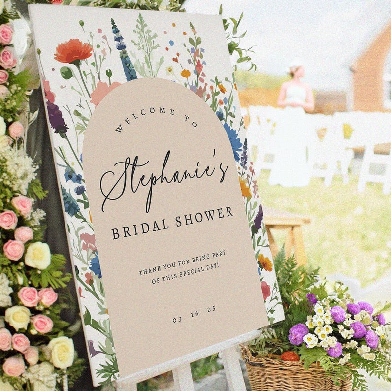 Puede incluir: Un letrero de bienvenida rectangular con un borde de flores silvestres coloridas y un arco beige central. El texto dice: Welcome to Stephanie's BRIDAL SHOWER, THANK YOU FOR BEING PART OF THIS SPECIAL DAY!, y la fecha 03 16 25 en negro.