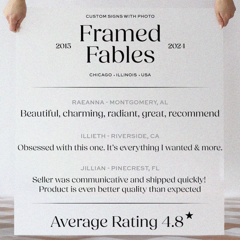 K&ouml;nnte beinhalten: Ein wei&szlig;es Schild, das von H&auml;nden gehalten wird, mit dem Text "Framed Fables" und den Jahren 2015 und 2024. Kundenbewertungen und eine durchschnittliche Bewertung von 4,8 Sternen werden darunter angezeigt. Das Schild enth&auml;lt auch den Text "CUSTOM SIGNS WITH PHOTO".