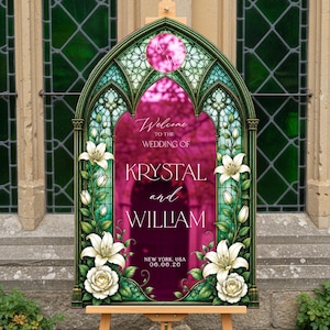 K&ouml;nnte beinhalten: Ein bogenf&ouml;rmiges Hochzeitsschild mit einem Buntglasrahmen-Design, verziert mit wei&szlig;en Lilien und Rosen. In der Mitte steht der Text: Welcome to the wedding of Krystal and William, New York, USA, 06.06.26, mit einem kreisf&ouml;rmigen Monogramm oben.
