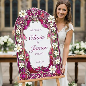 May include: An arched wedding sign featuring a stained glass pattern in shades of magenta and purple with white floral accents. The text reads: WELCOME TO Olivia & James WEDDING 03.04.26. The sign is mounted on a wooden easel stand.