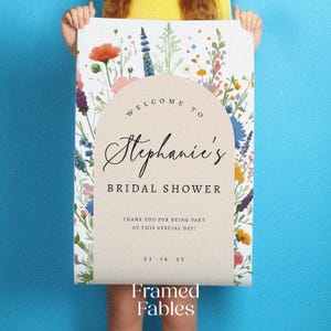 Puede incluir: Un letrero rectangular con un arco beige central que contiene el texto "WELCOME TO Stephanie's BRIDAL SHOWER THANK YOU FOR BEING PART OF THIS SPECIAL DAY! 03 16 25". El borde est&aacute; decorado con coloridas ilustraciones de flores silvestres.