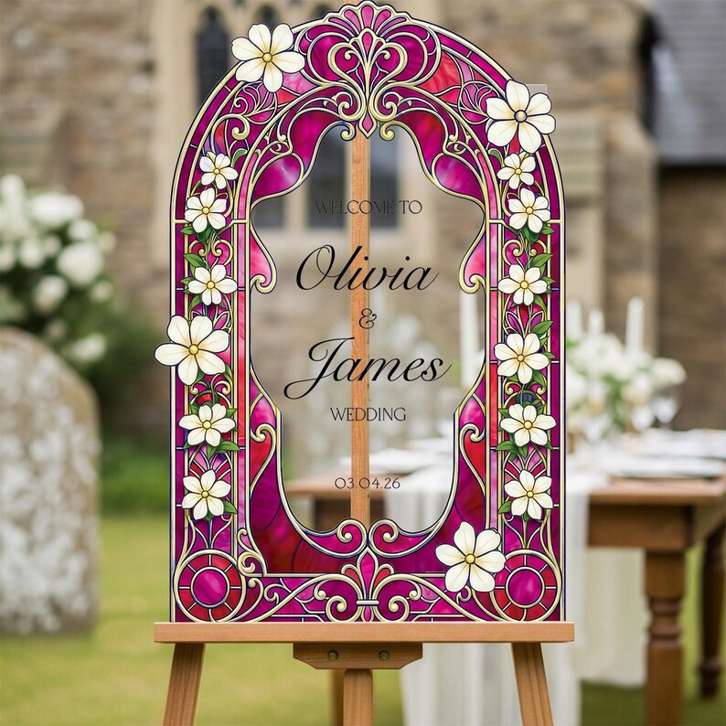 May include: An arched wedding sign featuring a stained glass pattern in shades of magenta and red with white floral accents. The text reads: WELCOME TO Olivia & James WEDDING 03.04.26. The sign is mounted on a wooden easel stand.