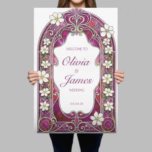 May include: A rectangular wedding welcome sign featuring a magenta and gold stained glass arch frame decorated with white flowers. The centre text reads: WELCOME TO Olivia & James WEDDING 03.04.26 in a mix of serif and script fonts.