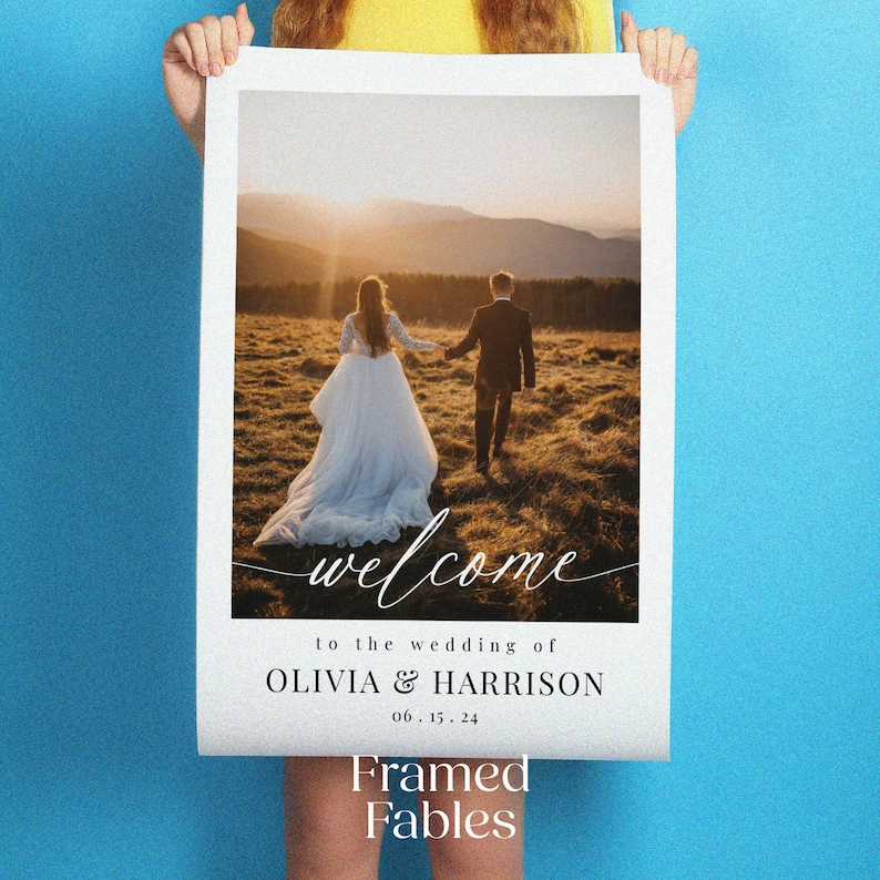 May include: A wedding welcome sign with a photo of a couple walking away from the camera in a field. The sign says "Welcome to the wedding of Olivia & Harrison 06.15.24" and "Framed Fables".