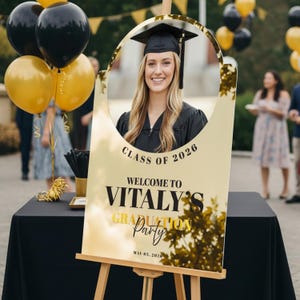 K&ouml;nnte beinhalten: Goldenes Schild f&uuml;r eine Abschlussfeier mit einem Foto einer l&auml;chelnden Absolventin in Robe und Hut. Auf dem Schild steht "Class of 2026" und "Welcome to Vitaly's Graduation Party".