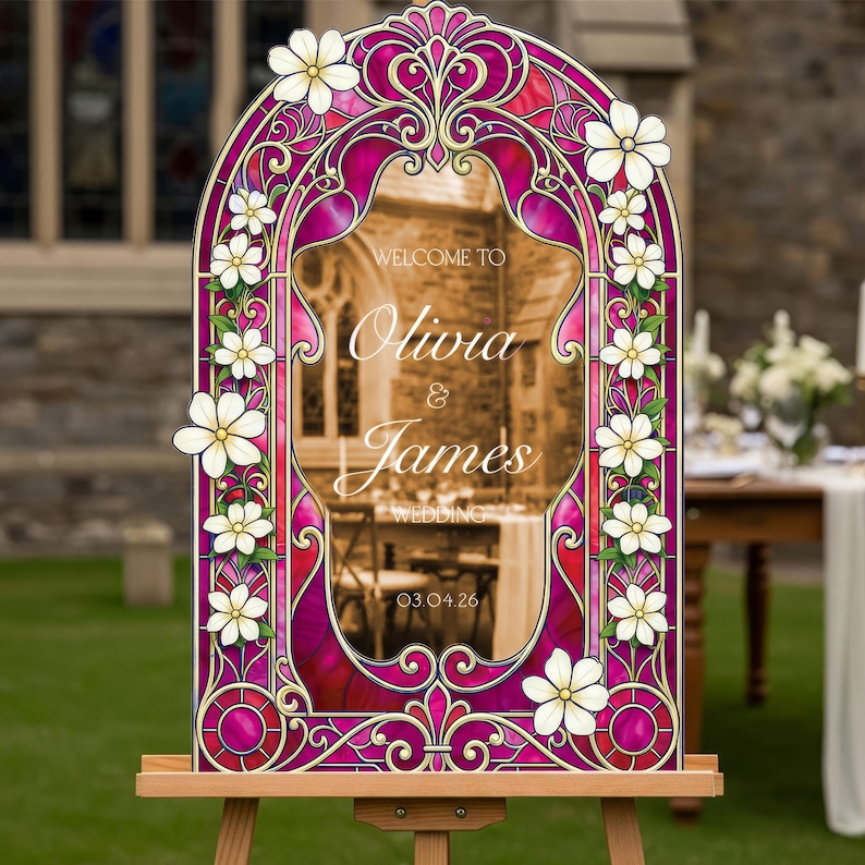 May include: An arched wedding welcome sign featuring a vibrant magenta and purple stained glass pattern with white floral accents. The centre text reads: WELCOME TO Olivia & James WEDDING 03.04.26. The sign is displayed on a wooden easel stand.
