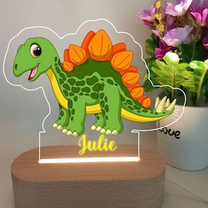May include: A wooden night light with a clear acrylic insert featuring a cartoon green dinosaur with orange spikes. The dinosaur's name, "Julie", is printed in yellow on the base of the night light.