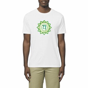 Peut inclure: Un t-shirt blanc avec un graphique vert et turquoise représentant l'Anahata chakra, le chakra du cœur, avec le symbole sanskrit "Ya" au centre.