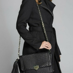 Puede incluir: Un bolso de hombro acolchado negro con una correa de cadena dorada y un borla. El bolso tiene un patrón de chevron y un cierre de solapa con una hebilla dorada.
