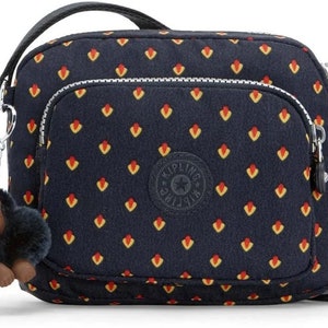 Peut inclure: Un petit sac bandoulière bleu avec un motif géométrique rouge et jaune. Le sac a une fermeture éclair et un petit porte-clés en forme de singe.