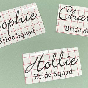 May include: Three white labels with black text on a green background. The labels read "Sophie Bride Squad", "Charley Bride Squad", and "Hollie Bride Squad".