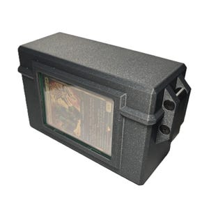 May include: A rectangular, matte black storage box with a textured finish, featuring a clear display window on the front side. A single trading card is visible inside the window, secured by a frame. The box has a hinged design with visible screws.